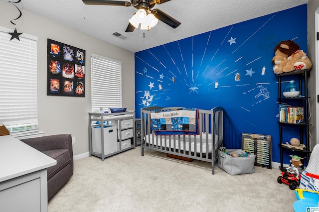 carpeted bedroom featuring a nursery area, a textured ceiling, and ceiling fan