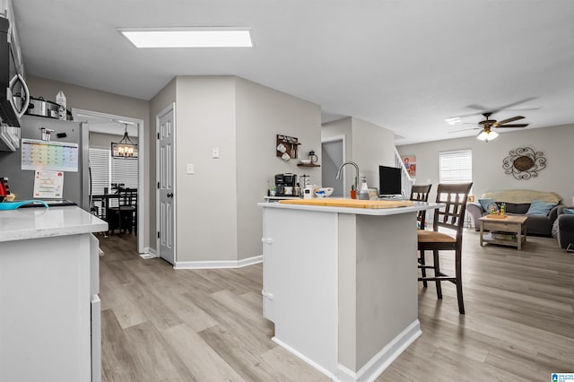 kitchen with light wood-type flooring, a kitchen bar, and ceiling fan