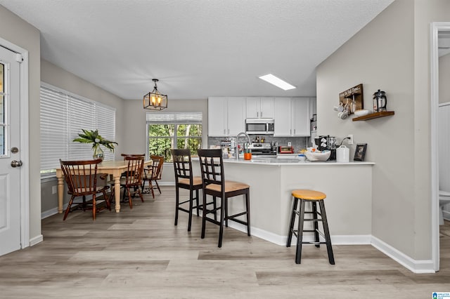 kitchen featuring white cabinets, kitchen peninsula, a breakfast bar area, light hardwood / wood-style flooring, and appliances with stainless steel finishes