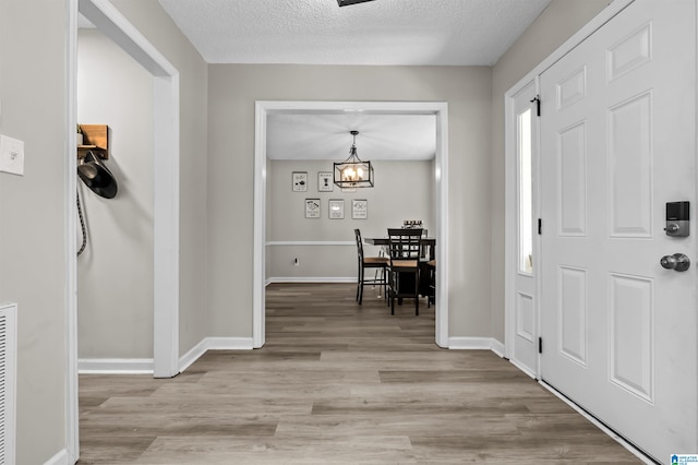 entrance foyer featuring an inviting chandelier, a textured ceiling, and light wood-type flooring