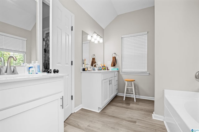 bathroom featuring hardwood / wood-style floors, a tub to relax in, vaulted ceiling, and vanity