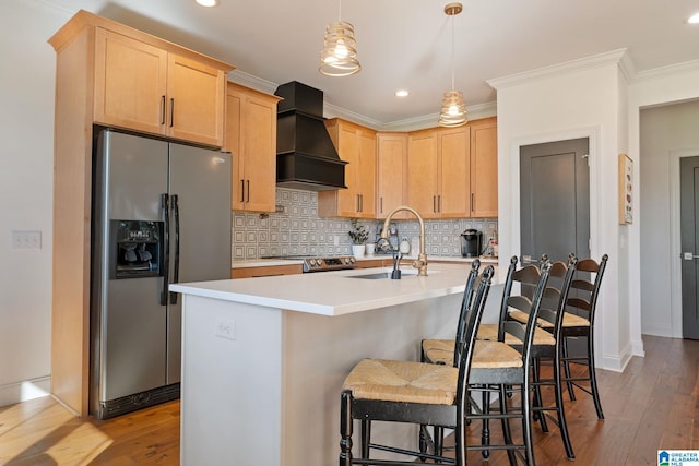 kitchen featuring appliances with stainless steel finishes, light brown cabinetry, premium range hood, and an island with sink