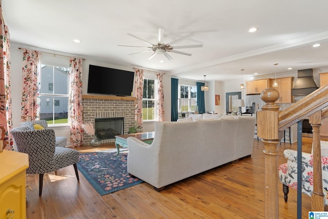 living room with ceiling fan, light wood-type flooring, a brick fireplace, and ornamental molding