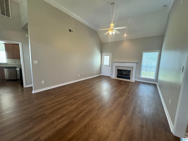 unfurnished living room with a tiled fireplace, ceiling fan, dark wood-type flooring, ornamental molding, and high vaulted ceiling