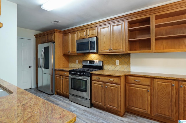 kitchen with light hardwood / wood-style floors, appliances with stainless steel finishes, light stone counters, and backsplash