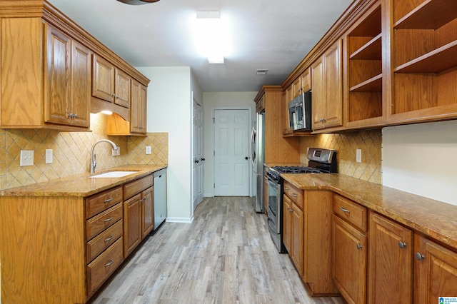 kitchen with light stone countertops, appliances with stainless steel finishes, sink, light wood-type flooring, and backsplash