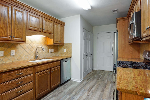 kitchen with tasteful backsplash, appliances with stainless steel finishes, light stone countertops, light wood-type flooring, and sink