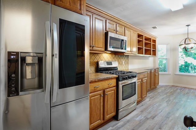 kitchen featuring appliances with stainless steel finishes, pendant lighting, a notable chandelier, decorative backsplash, and light hardwood / wood-style flooring