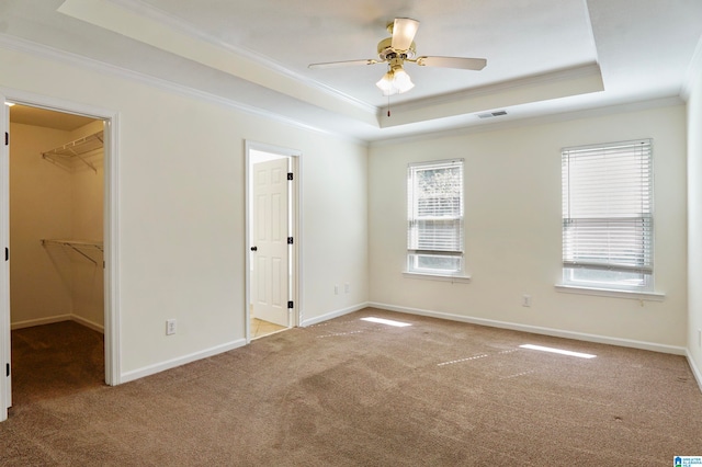 unfurnished bedroom with a closet, a raised ceiling, multiple windows, and a walk in closet