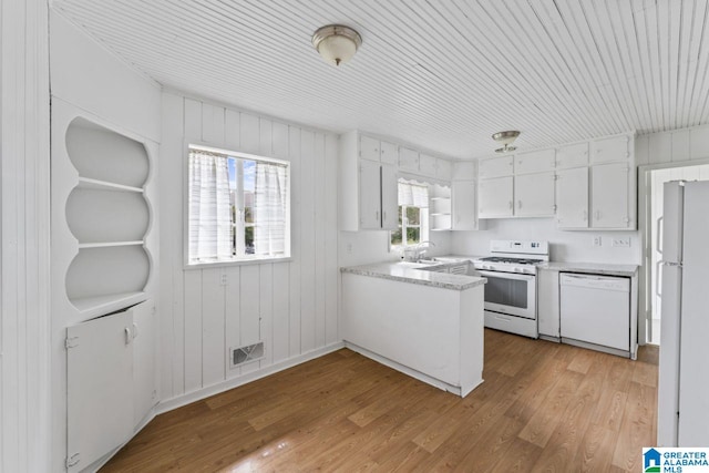 kitchen with light hardwood / wood-style flooring, sink, white cabinetry, white appliances, and wood walls