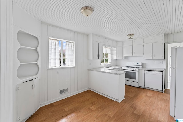 kitchen with wooden walls, white cabinets, light wood-type flooring, and white appliances