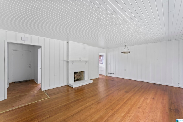 unfurnished living room with wood-type flooring and a brick fireplace