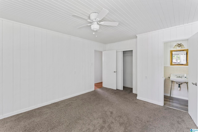 unfurnished bedroom featuring a closet, dark carpet, ensuite bath, sink, and ceiling fan