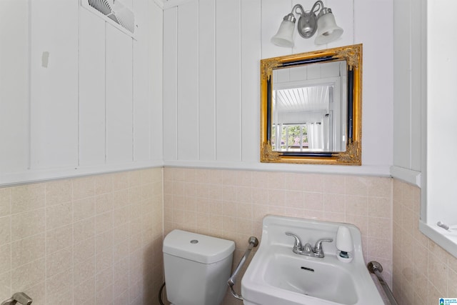 bathroom with toilet, sink, and tile walls