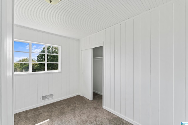 unfurnished bedroom featuring a closet, wood walls, and carpet