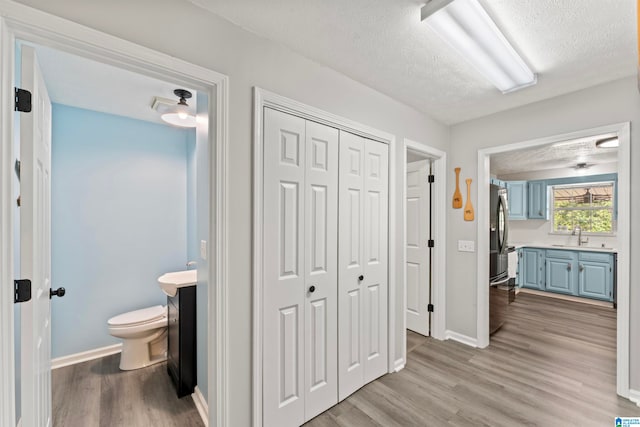 corridor with a textured ceiling, light hardwood / wood-style flooring, and sink