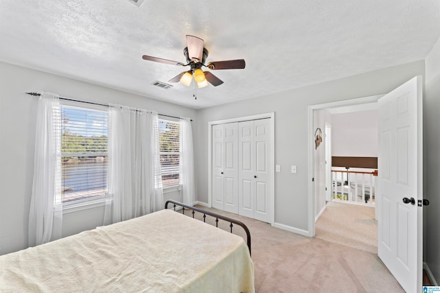 bedroom with ceiling fan, a textured ceiling, a closet, and light carpet