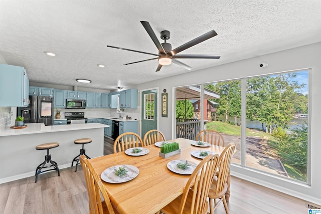 dining area featuring ceiling fan, sink, light hardwood / wood-style floors, and a textured ceiling