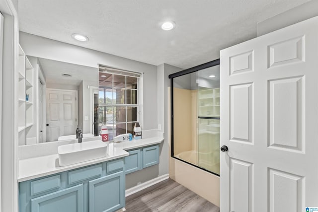 bathroom with vanity, shower / bath combination with glass door, wood-type flooring, and a textured ceiling