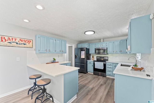 kitchen featuring appliances with stainless steel finishes, kitchen peninsula, sink, and light hardwood / wood-style flooring