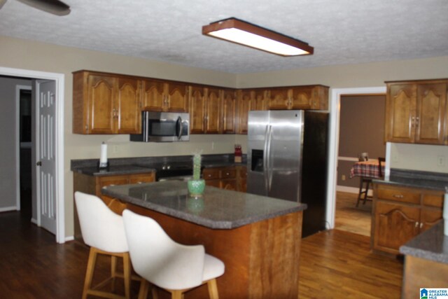 kitchen with a kitchen island, a textured ceiling, dark wood-type flooring, stainless steel appliances, and a breakfast bar