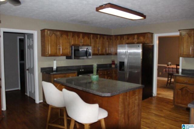 kitchen with a center island, a breakfast bar, dark hardwood / wood-style flooring, appliances with stainless steel finishes, and a textured ceiling