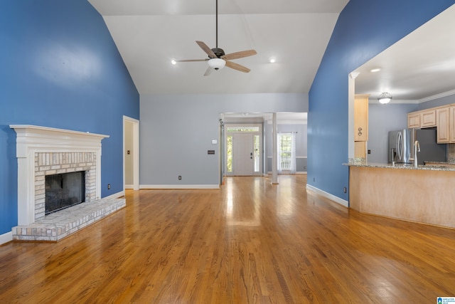 unfurnished living room with light hardwood / wood-style floors, ceiling fan, high vaulted ceiling, and a brick fireplace