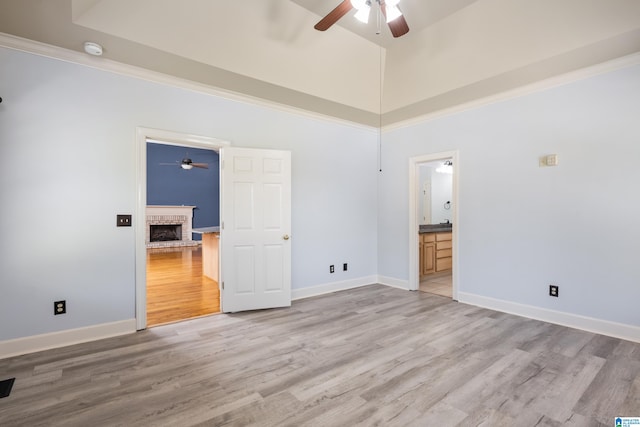 unfurnished bedroom with ensuite bathroom, a towering ceiling, a fireplace, ceiling fan, and hardwood / wood-style flooring