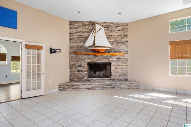 unfurnished living room featuring a stone fireplace, french doors, a towering ceiling, and light tile patterned floors