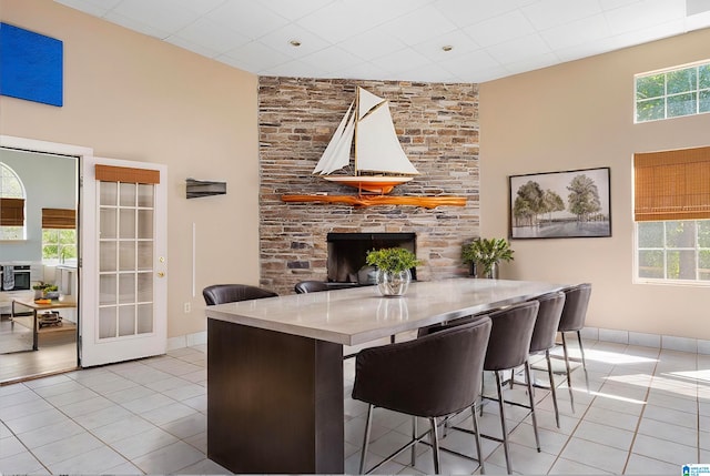 dining area featuring a wealth of natural light, light tile patterned flooring, a stone fireplace, and a towering ceiling