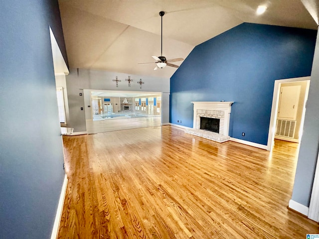 unfurnished living room featuring hardwood / wood-style floors, ceiling fan, high vaulted ceiling, and a brick fireplace