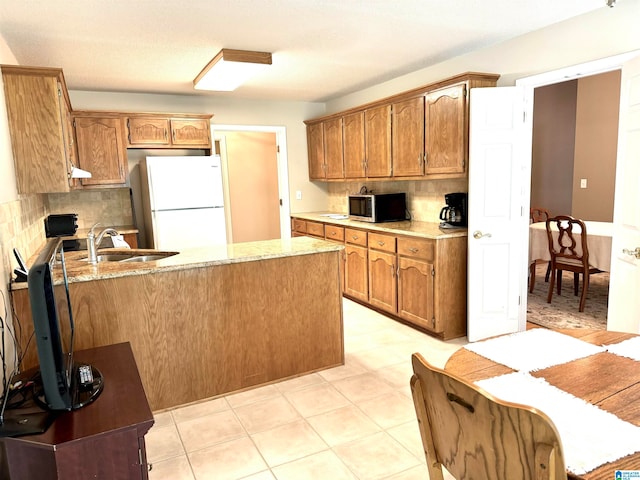 kitchen with light stone countertops, decorative backsplash, white refrigerator, and sink