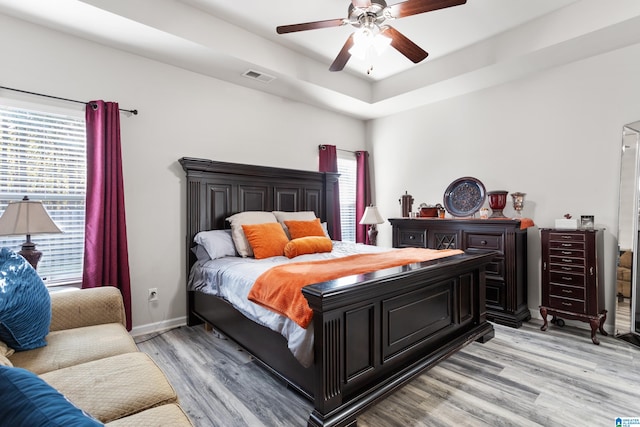 bedroom featuring light hardwood / wood-style floors, a tray ceiling, and ceiling fan