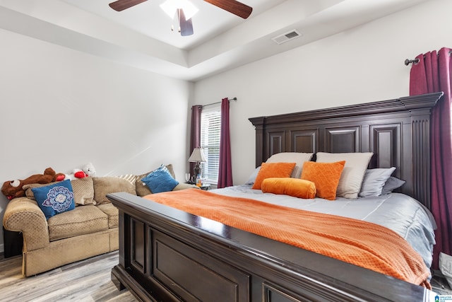 bedroom featuring light hardwood / wood-style flooring, a raised ceiling, and ceiling fan