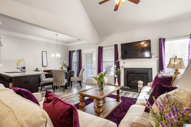 living room with wood-type flooring, sink, ceiling fan with notable chandelier, vaulted ceiling, and ornamental molding