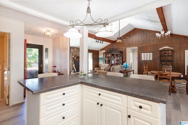 kitchen with wooden walls, decorative light fixtures, lofted ceiling with beams, and light wood-type flooring