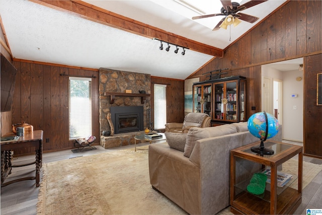 living room with a stone fireplace, vaulted ceiling with beams, wooden walls, and light hardwood / wood-style flooring