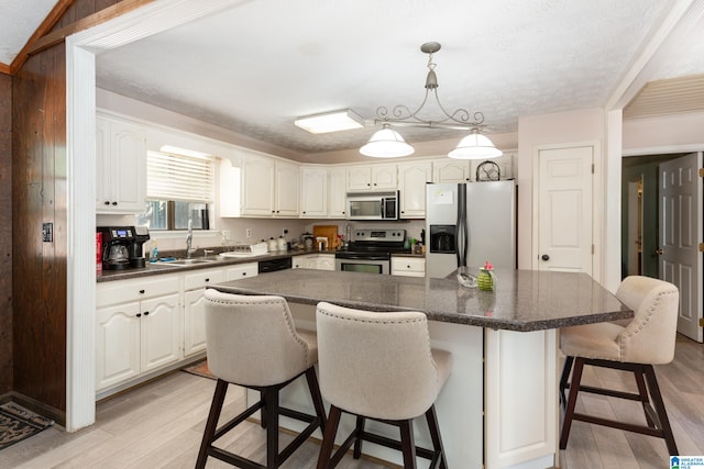 kitchen with appliances with stainless steel finishes, a kitchen island, white cabinetry, and light hardwood / wood-style flooring