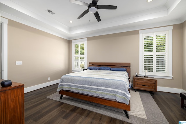 bedroom with ceiling fan, a tray ceiling, dark hardwood / wood-style flooring, and multiple windows