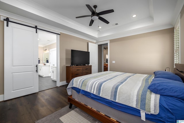 bedroom with a barn door, ceiling fan, a tray ceiling, dark hardwood / wood-style flooring, and ensuite bath