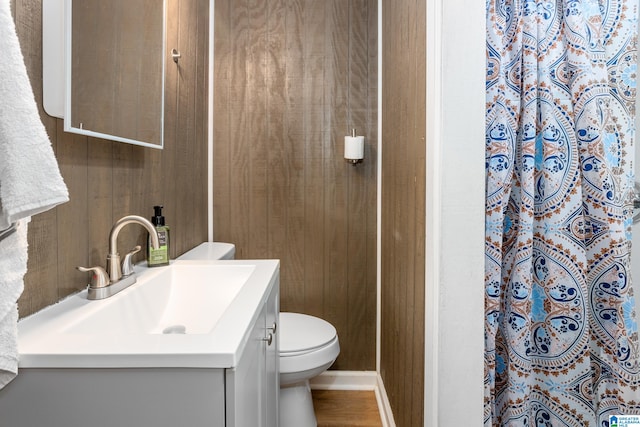 bathroom featuring wooden walls, hardwood / wood-style floors, walk in shower, vanity, and toilet