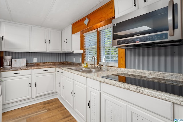 kitchen featuring black electric stovetop, sink, light wood-type flooring, and white cabinetry