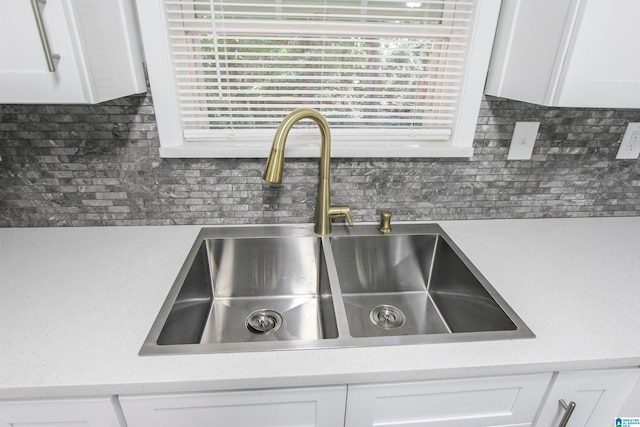 details featuring backsplash, light stone countertops, sink, and white cabinets