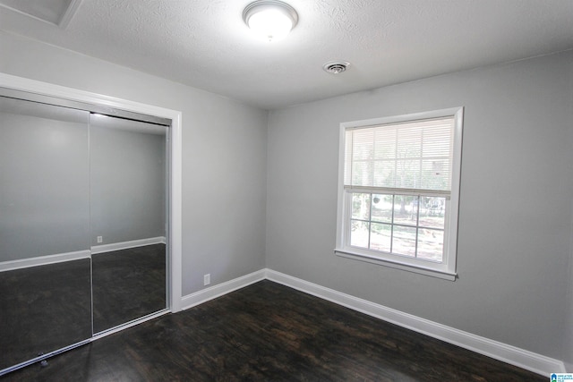 unfurnished bedroom with dark hardwood / wood-style floors, a textured ceiling, and a closet