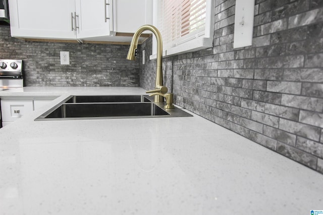 kitchen featuring decorative backsplash, sink, white cabinets, and stove