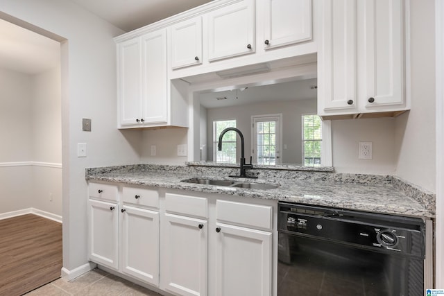 kitchen with light wood-type flooring, black dishwasher, sink, light stone counters, and white cabinets