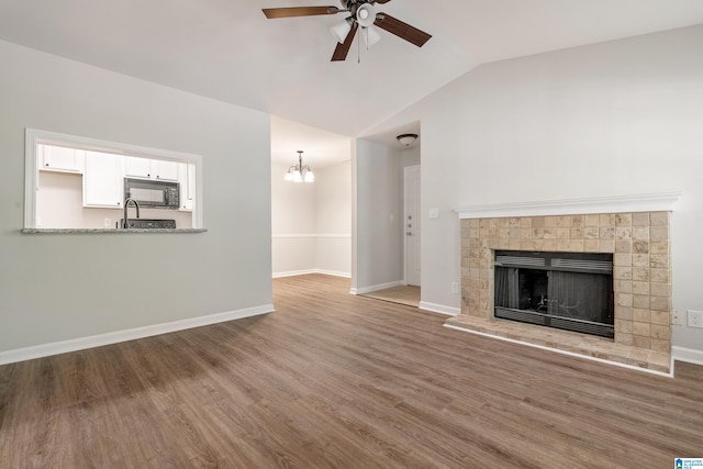 unfurnished living room with ceiling fan with notable chandelier, vaulted ceiling, and hardwood / wood-style flooring