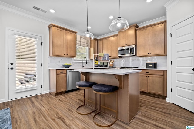 kitchen with hardwood / wood-style floors, a center island, stainless steel appliances, hanging light fixtures, and ornamental molding