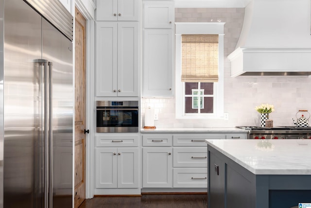 kitchen with decorative backsplash, white cabinets, custom exhaust hood, and appliances with stainless steel finishes