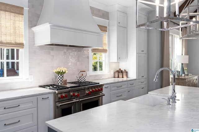 kitchen featuring decorative backsplash, custom exhaust hood, sink, range with two ovens, and white cabinetry